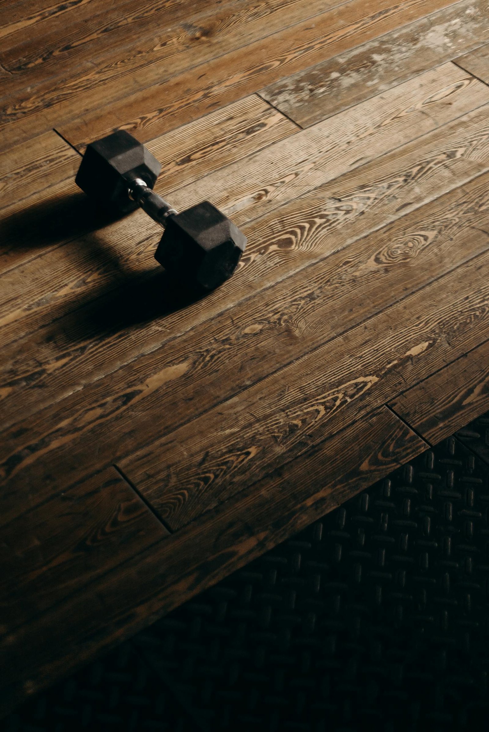 A solitary dumbbell rests on a wooden gym floor, offering ample copy space.