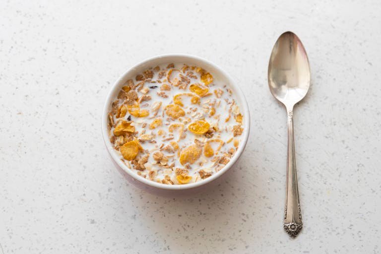 Breakfast cereal with milk in a bowl alongside a spoon on a white table.