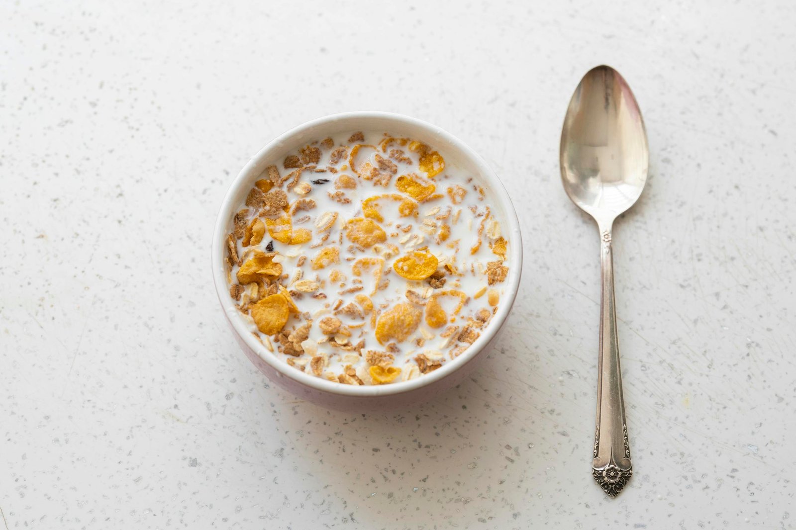 Breakfast cereal with milk in a bowl alongside a spoon on a white table.