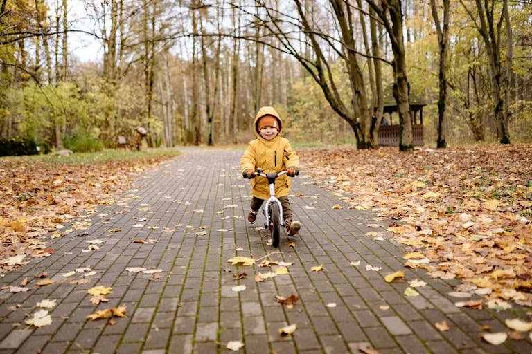 Smiling child riding a bike on a leaf-covered path in an autumn park, experiencing joy and fun.